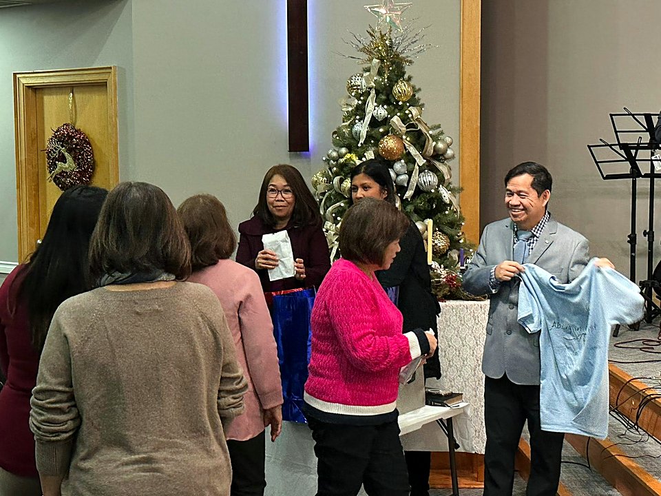 Church members exchanging gifts beside the Christmas tree after a service