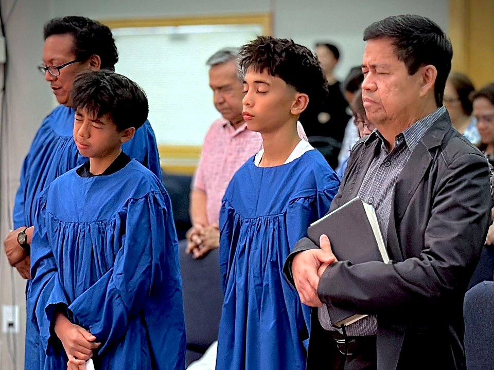 Two young men in blue baptism robes standing in prayer during a service