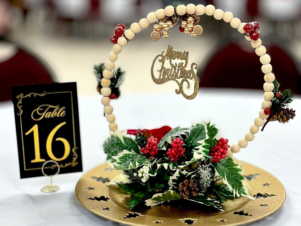 A Christmas centrepiece with holly, berries and a Merry Christmas sign on a party table